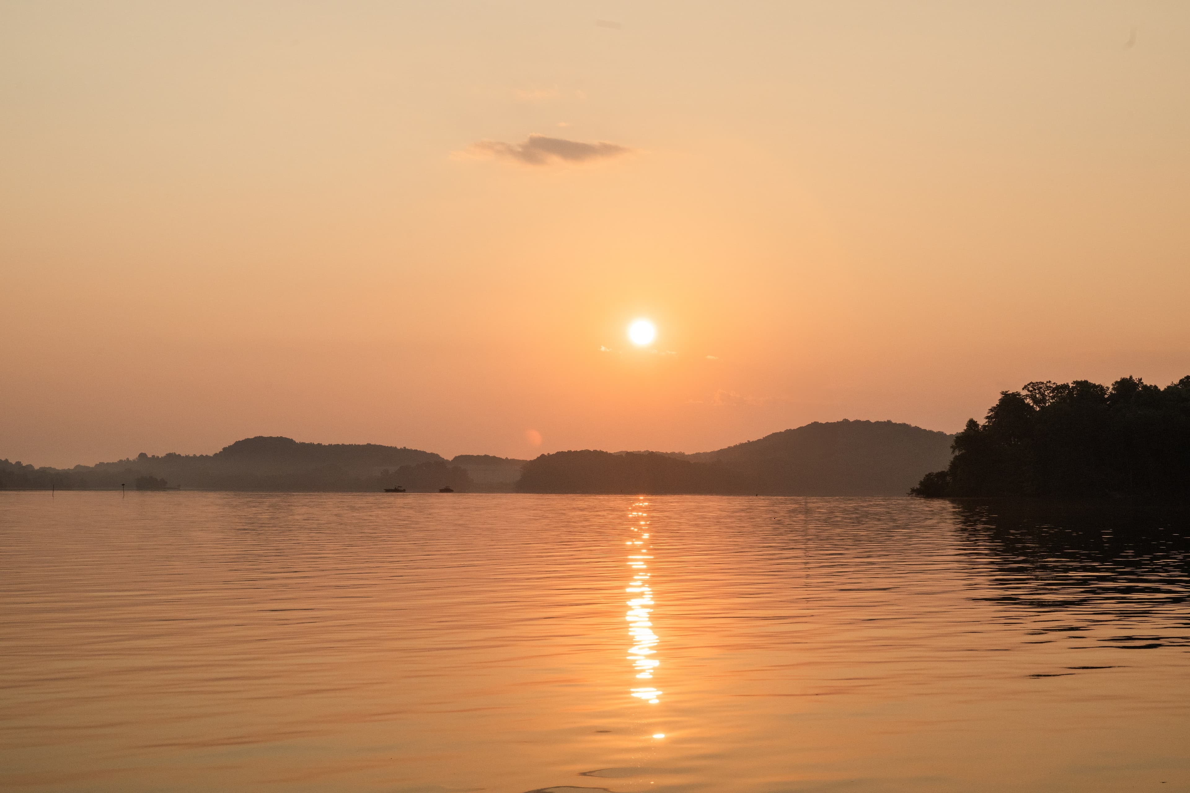 Peaceful sunset over a lake with golden reflections on calm water and hills silhouetted in the background.