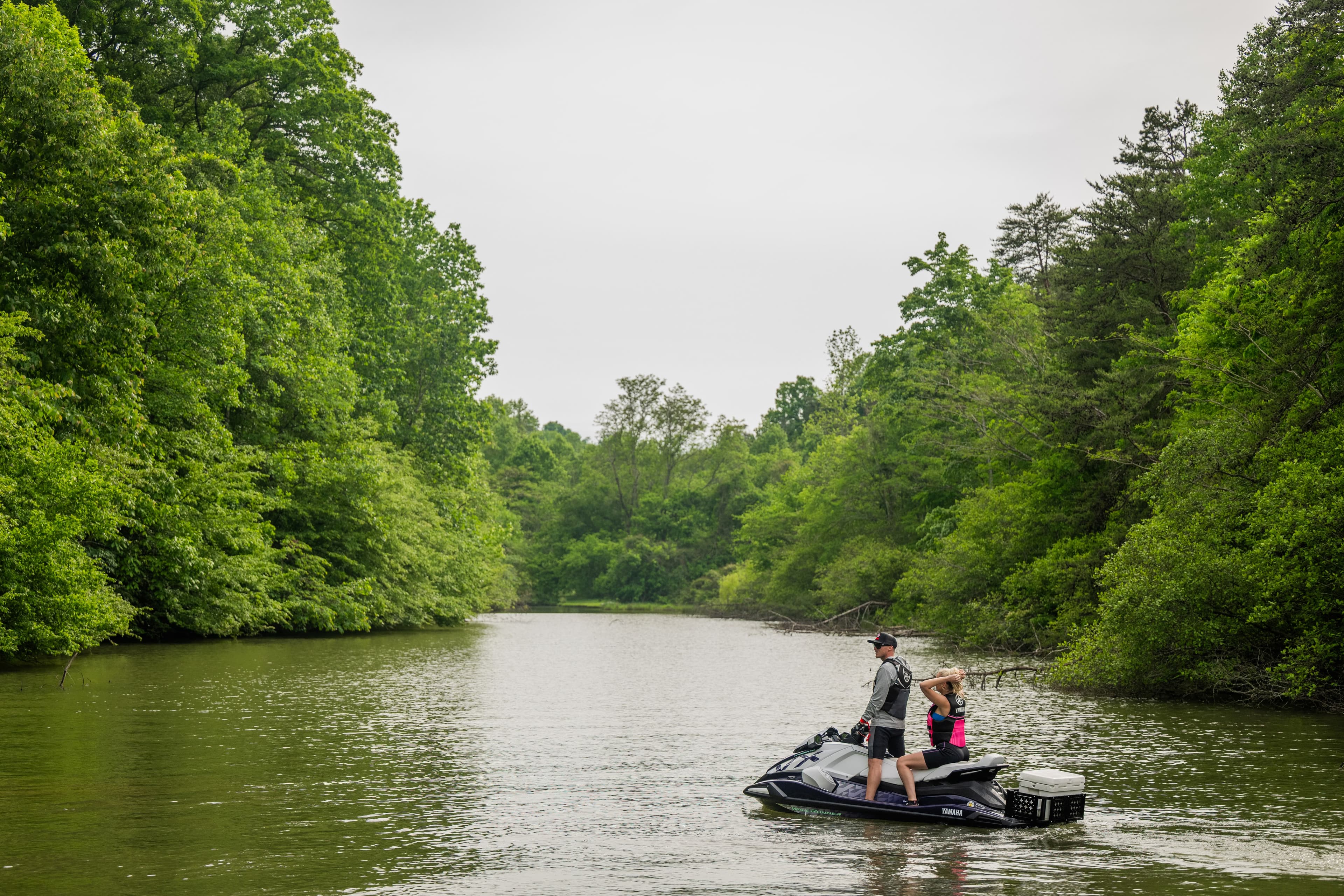 Black Yamaha jet ski with two riders on a tree-lined river