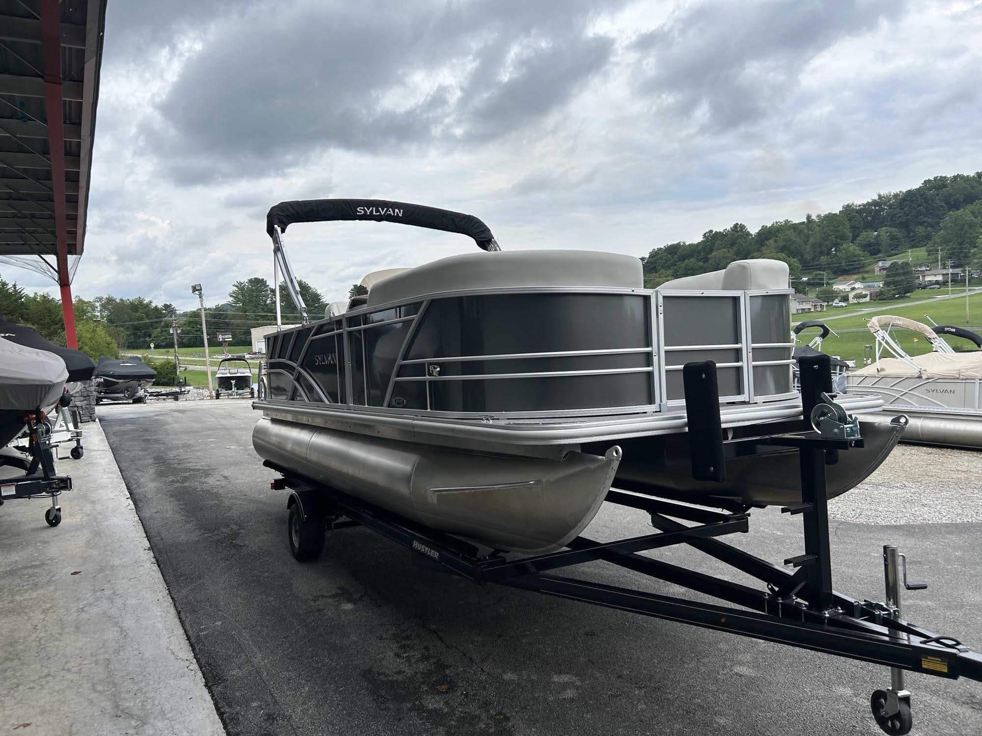 A new 2026 Sylvan R22 CLZ DH pontoon boat, gray in color, is shown on a gravel lot at a dealership.